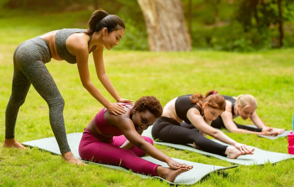 Young female yoga instructor teaching group of sporty women to do asanas correctly, outside